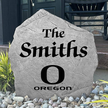 Custom University of Oregon Name Stone displayed in a landscaped flower bed, showcasing personalized family lettering and officially licensed Oregon Ducks artwork. This decorative outdoor stone creates a beautiful focal point for alumni homes and Oregon fans.