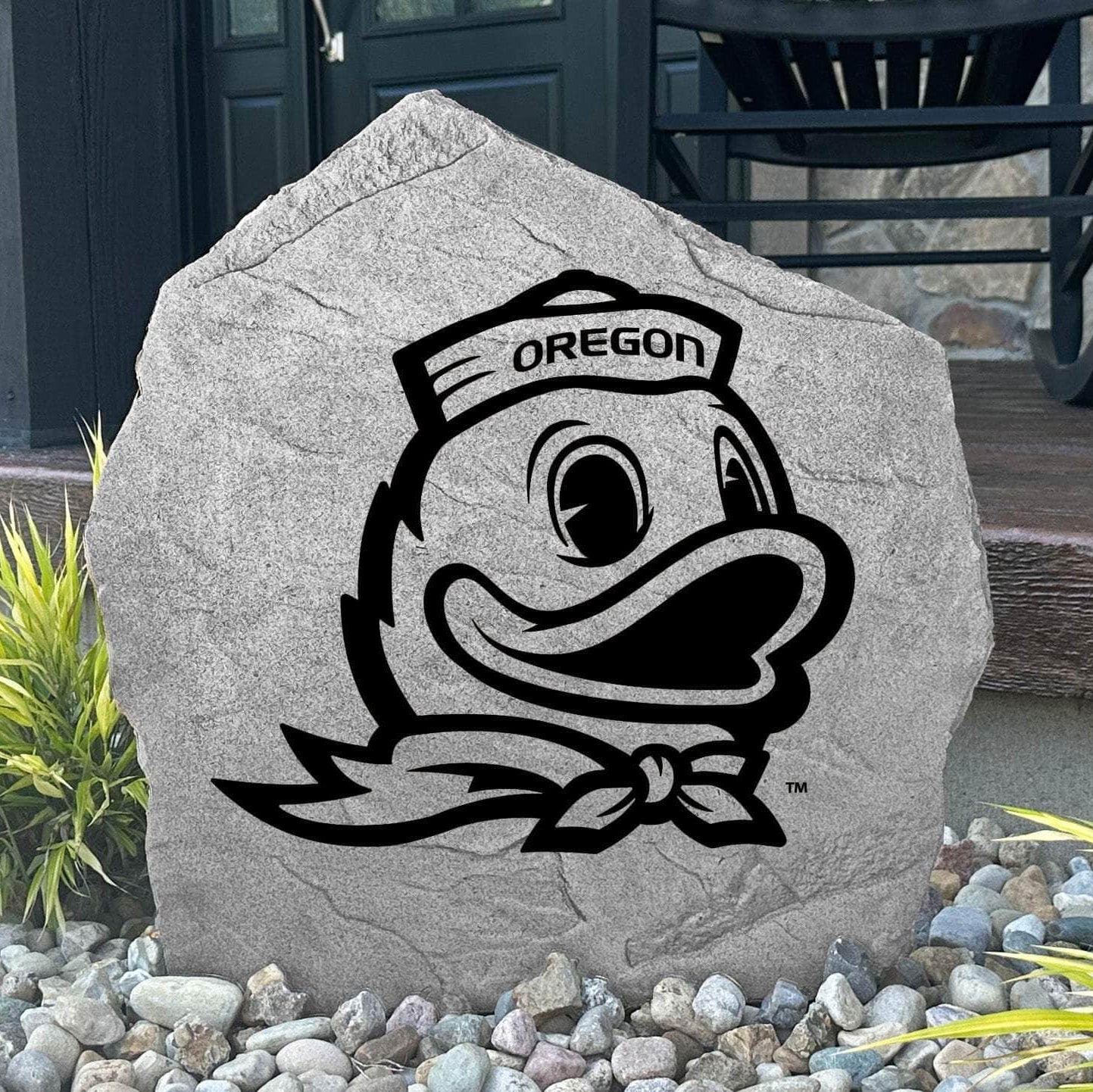Custom Oregon Ducks Logo Stone displayed in a landscaped flower bed, showcasing officially licensed Duck mascot artwork with permanent engraving. This decorative outdoor stone creates a striking focal point for alumni homes and Oregon fans.
