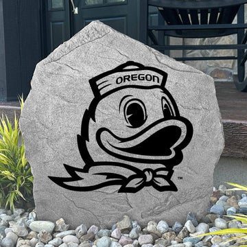 Custom Oregon Ducks Logo Stone displayed in a landscaped flower bed, showcasing officially licensed Duck mascot artwork with permanent engraving. This decorative outdoor stone creates a striking focal point for alumni homes and Oregon fans.