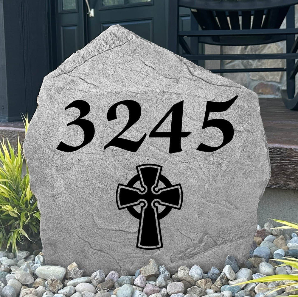Custom Celtic Cross Address Stone displayed in a landscaped flower bed, showcasing personalized house numbers and intricate Celtic detailing engraved directly into the stone surface. This elegant address marker creates a stunning focal point for the home.
