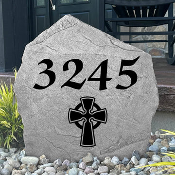 Custom Celtic Cross Address Stone displayed in a landscaped flower bed, showcasing personalized house numbers and intricate Celtic detailing engraved directly into the stone surface. This elegant address marker creates a stunning focal point for the home.