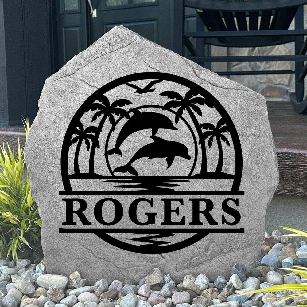 Custom Dolphin Palms Monogram Stone displayed in a landscaped flower bed, showcasing personalized engraving with elegant dolphins and palm trees. This engraved outdoor stone creates a beautiful focal point for walkways and coastal-inspired landscapes.