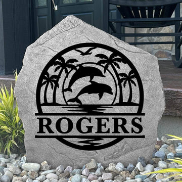 Custom Dolphin Palms Monogram Stone displayed in a landscaped flower bed, showcasing personalized engraving with elegant dolphins and palm trees. This engraved outdoor stone creates a beautiful focal point for walkways and coastal-inspired landscapes.