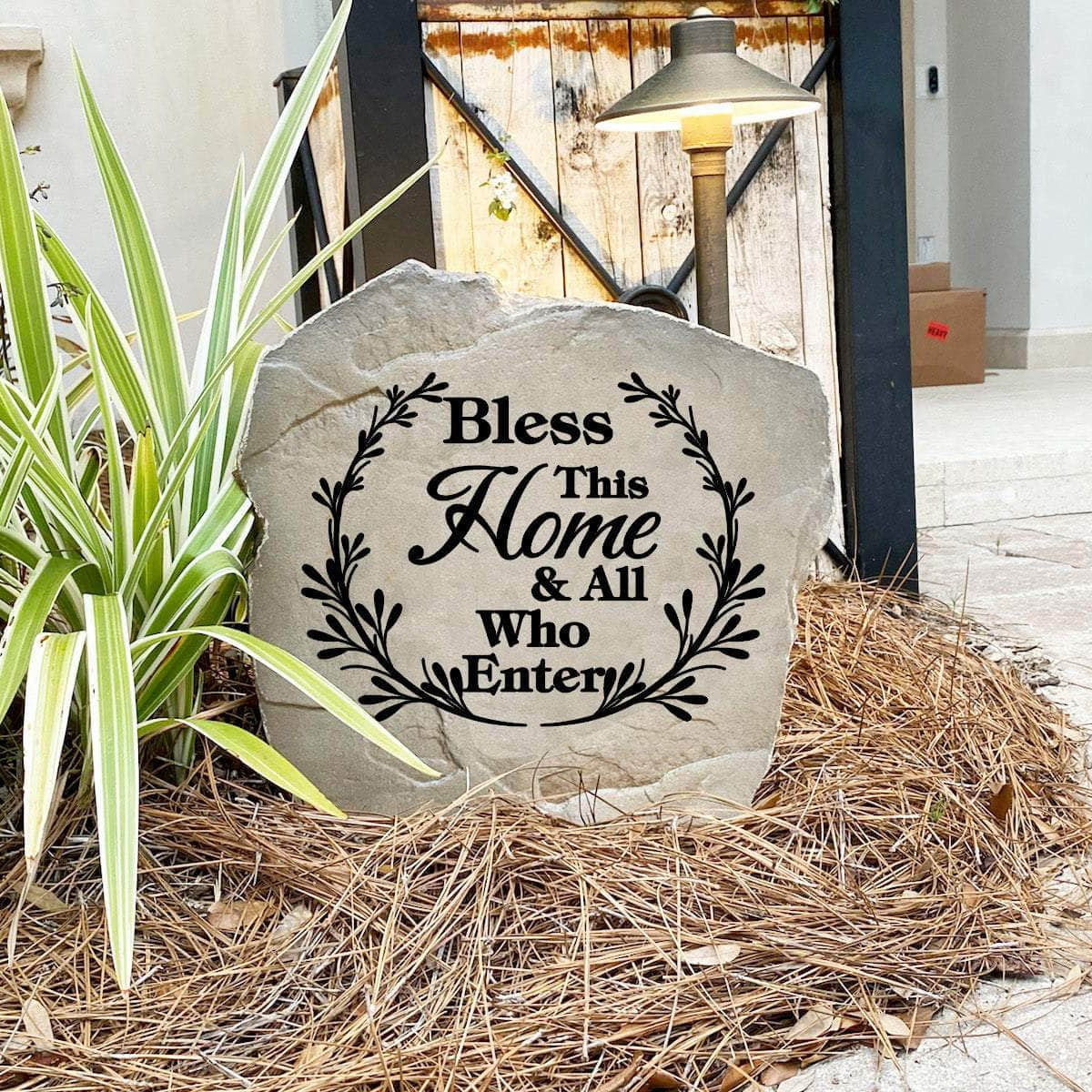 Faith-inspired Bless This Home & All Who Enter Stone nestled among colorful flowers and greenery, bringing peace and encouragement to front yard landscapes and outdoor living spaces.