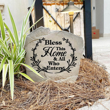Faith-inspired Bless This Home & All Who Enter Stone nestled among colorful flowers and greenery, bringing peace and encouragement to front yard landscapes and outdoor living spaces.