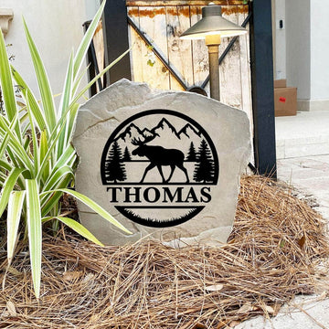 Engraved Moose Monogram Stone nestled among natural greenery and flowers, bringing rustic elegance and outdoor character to the landscape. Its weather-resistant design provides lasting beauty for patios and entryways.