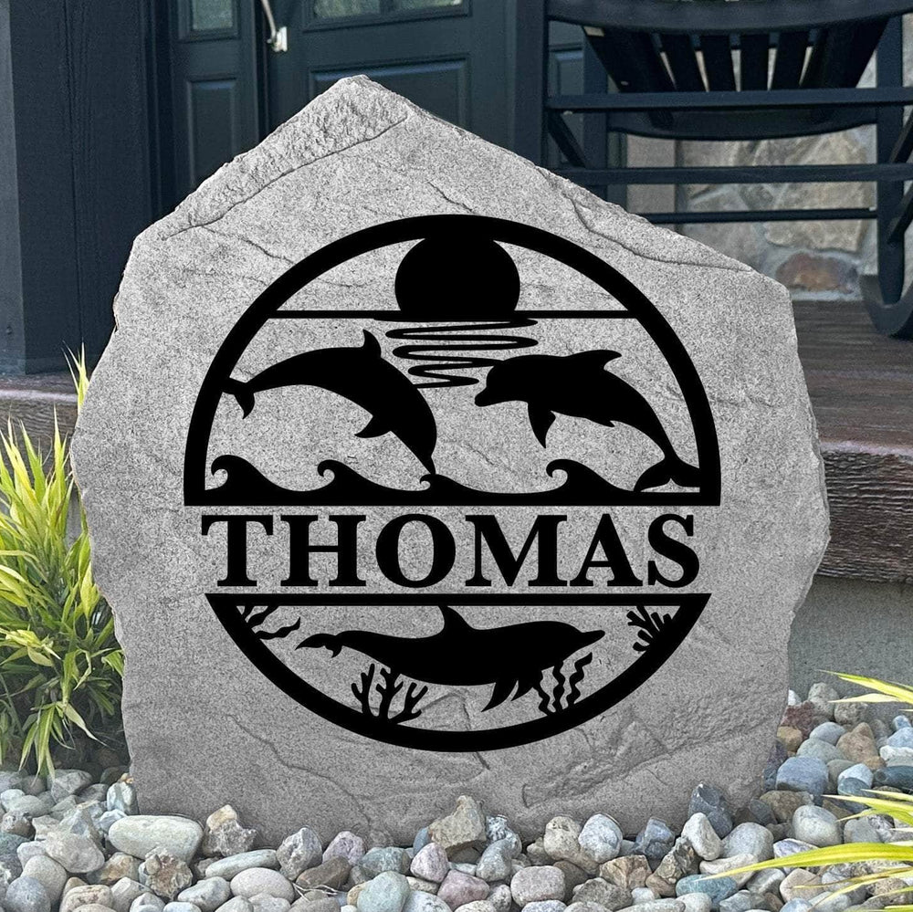 Custom Dolphin Monogram Stone displayed in a landscaped flower bed, showcasing personalized engraving and ocean-inspired dolphin artwork. This engraved outdoor stone creates a beautiful focal point for walkways and coastal homes.