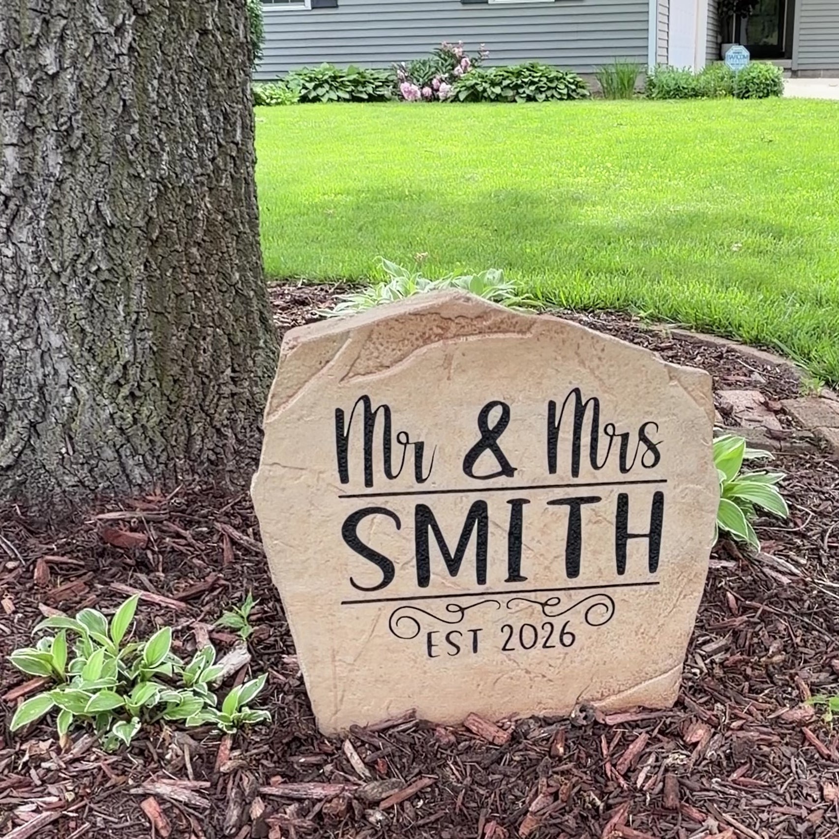 Engraved Mr. & Mrs. Name Stone nestled among colorful flowers and greenery, bringing charm and sophistication to front yard landscaping. This weather-resistant outdoor stone provides lasting beauty for patios and walkways.