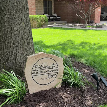 Engraved Grandma & Grandpa's House Stone nestled among colorful flowers and greenery, adding timeless beauty and inviting curb appeal to a grandparent's home. Perfect for gardens, patios, and front entrances.