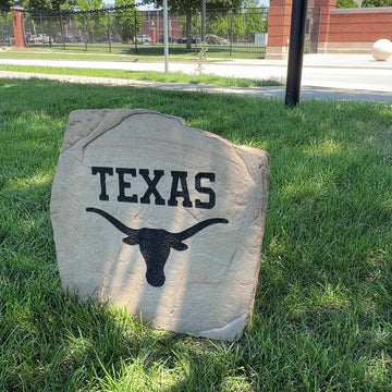 Custom Texas Longhorns Logo Stone displayed in a landscaped flower bed, showcasing officially licensed Texas Longhorns team artwork permanently engraved into the stone. This outdoor accent creates a bold focal point for Longhorns fans and outdoor living spaces.