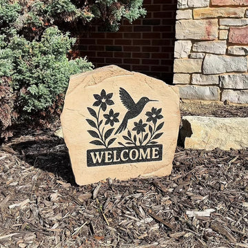 Custom Welcome Hummingbird Stone displayed in a landscaped garden, showcasing detailed hummingbird artwork and a warm welcome message. This engraved outdoor stone creates a beautiful focal point for walkways and home entrances.