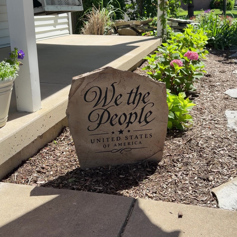 Framed by vibrant landscaping and natural stone, the We The People Stone features elegant engraved script inspired by America's founding principles. Its refined design creates a timeless statement piece that brings patriotic character and classic beauty to a front yard, garden, or entryway.