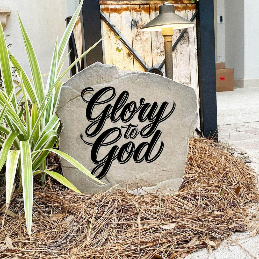 Faith-inspired Glory To God Stone nestled among colorful flowers and natural greenery, bringing encouragement and Christian décor to outdoor living spaces. Its weather-resistant design provides lasting beauty and inspiration.
