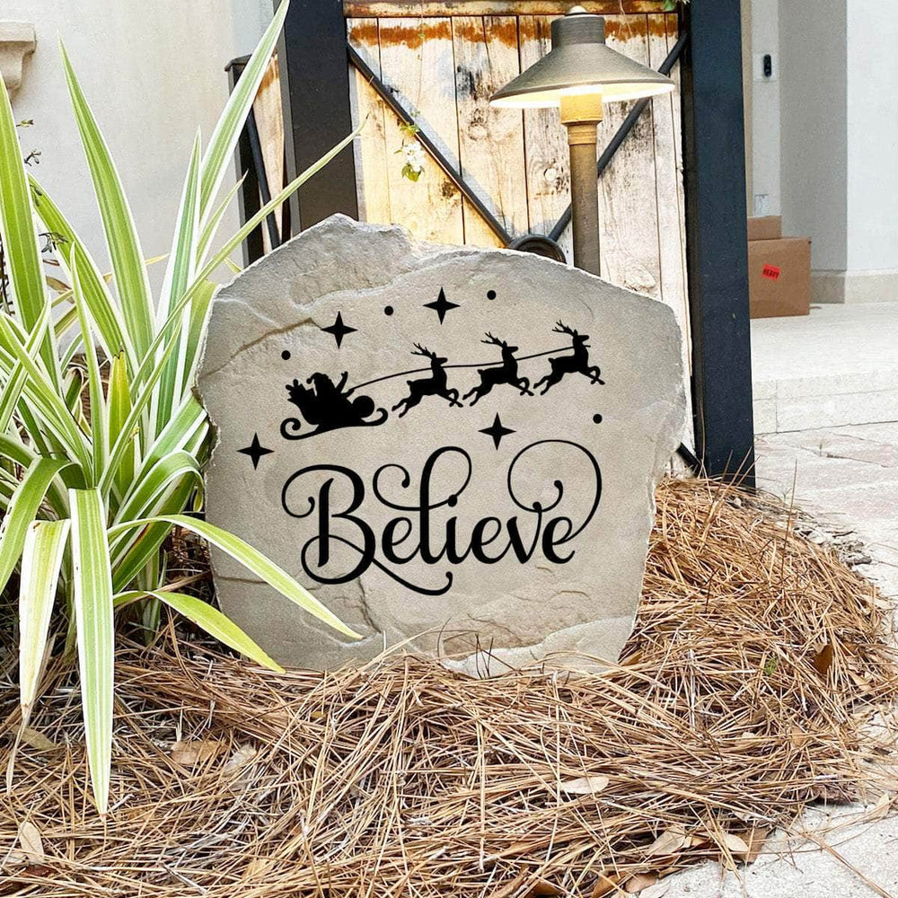 Decorative Believe Christmas Stone nestled among seasonal greenery and winter accents, bringing joy and inspiration to front yard landscapes and holiday displays. Its weather-resistant design provides lasting beauty throughout the season.
