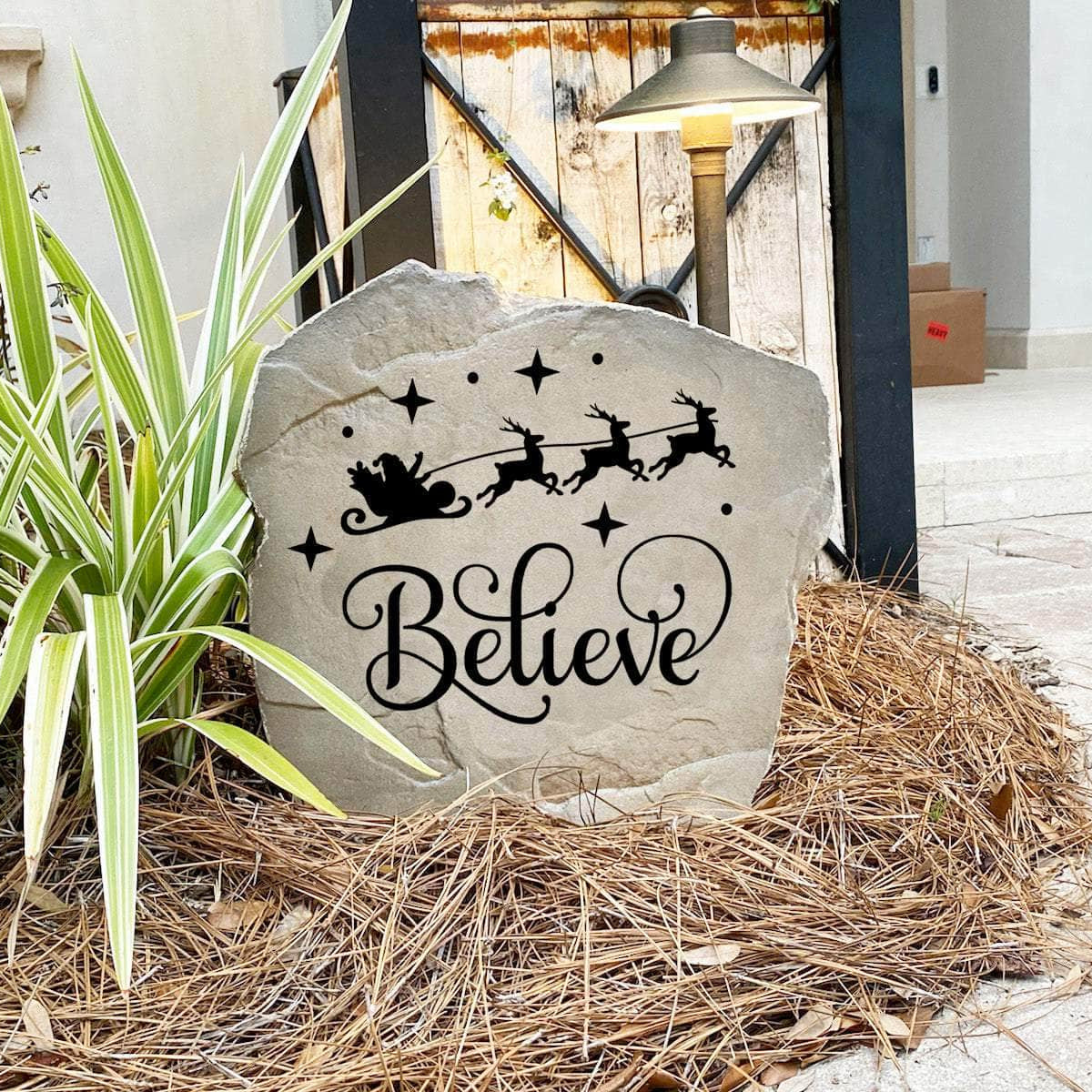 Decorative Believe Christmas Stone nestled among seasonal greenery and winter accents, bringing joy and inspiration to front yard landscapes and holiday displays. Its weather-resistant design provides lasting beauty throughout the season.