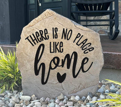 Engraved stone with the quote “There is no place like home” displayed in landscaping.