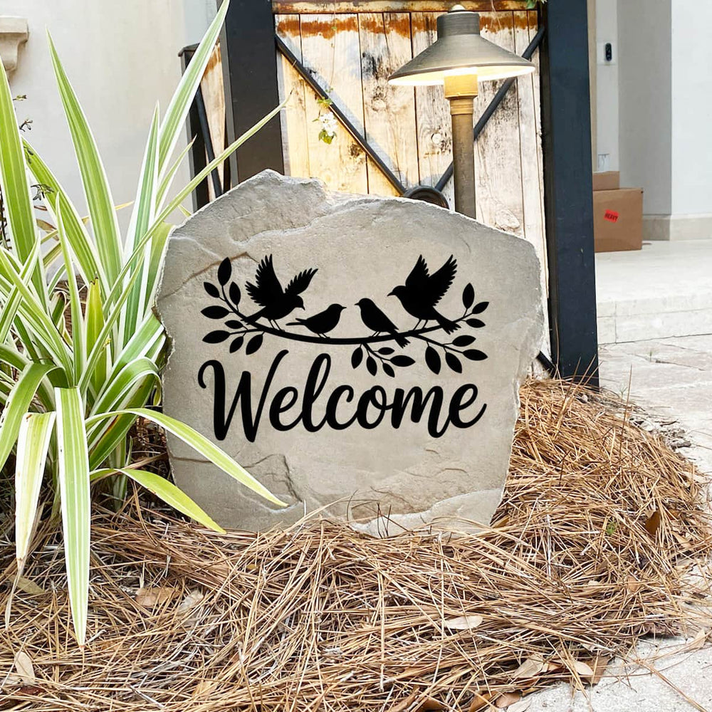 Decorative Welcome Bird Stone nestled among colorful flowers and greenery, bringing nature-inspired beauty to the landscape. The permanent engraving provides lasting durability and timeless style for any outdoor space.