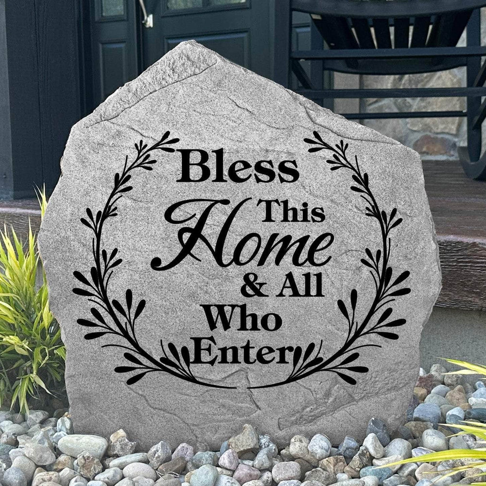 Bless This Home & All Who Enter Stone displayed in a landscaped flower bed, showcasing elegant engraving and a welcoming sentiment. This decorative outdoor stone creates a beautiful focal point for home entrances and walkways.