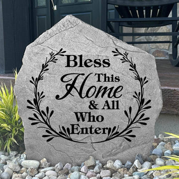 Bless This Home & All Who Enter Stone displayed in a landscaped flower bed, showcasing elegant engraving and a welcoming sentiment. This decorative outdoor stone creates a beautiful focal point for home entrances and walkways.